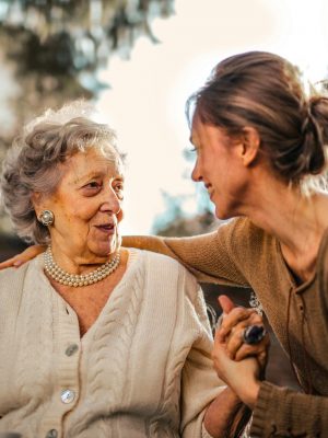 Elderly woman and adult daughter share a joyful, affectionate moment in a sunny garden.
